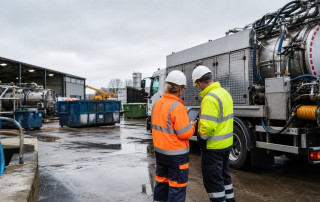 Waste and drainage operatives checking receipt information on a tablet beside a tanker